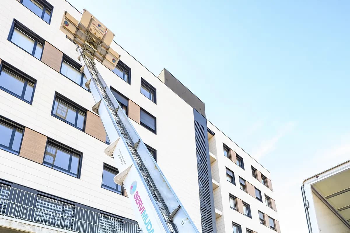 Camión de mudanza Servimudanzas con elevador desplegado a balcón de edificio